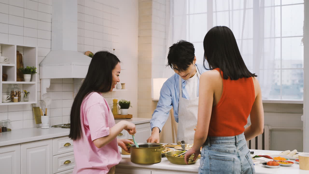 無料 ストック動画 - キッチンで料理をしたり、話したり、笑ったりしながら、鍋に材料を注ぐ 3 人の日本人の友人